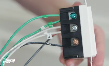 Checking the electrical wiring behind a smart dimmer switch with a tester.