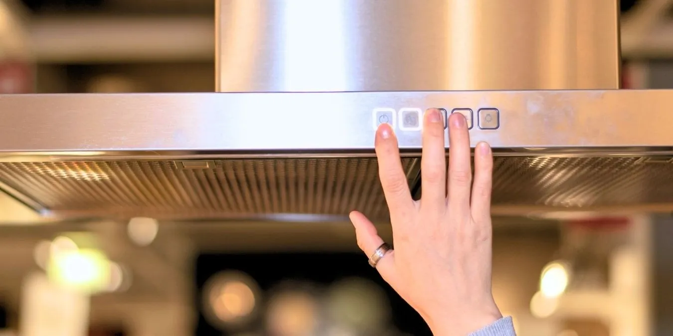Pressing the digital control panel buttons on a stainless steel range hood.