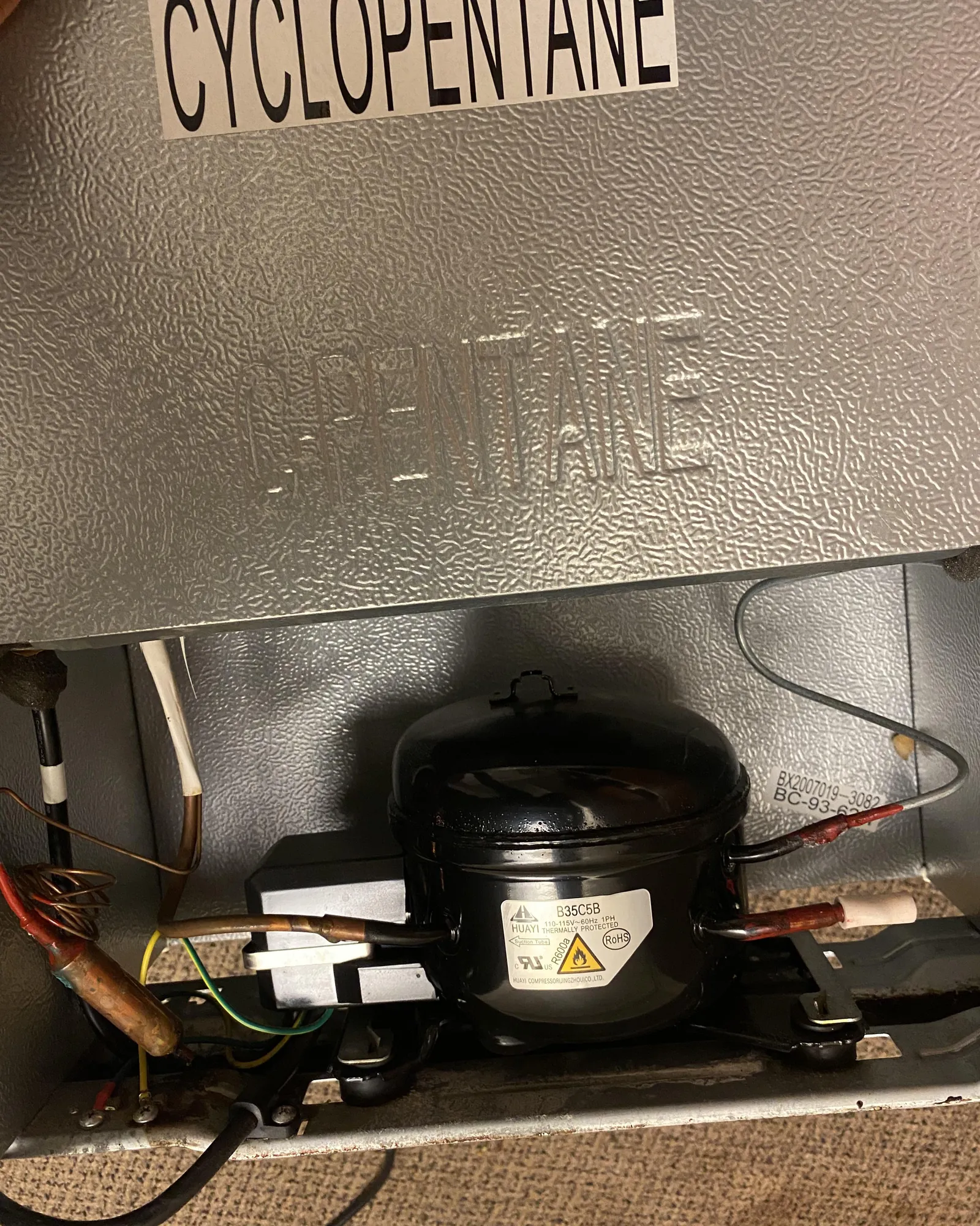 Dusty condenser coils on the back of a mini fridge need cleaning.