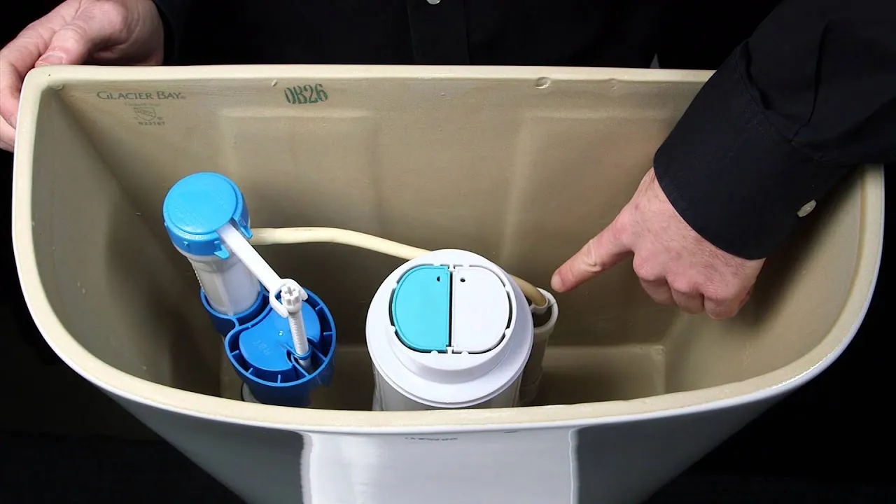 Hands adjusting the cable tension inside a dual flush toilet tank with a screwdriver.