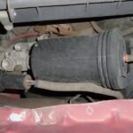 A modern SUV showing signs of a faulty air suspension system in a garage.