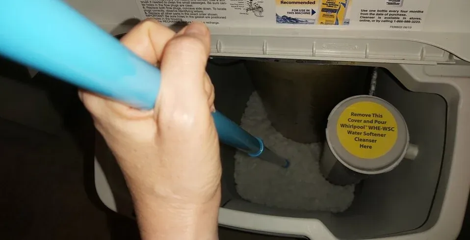 A person breaking up a hard salt crust inside a water softener brine tank.