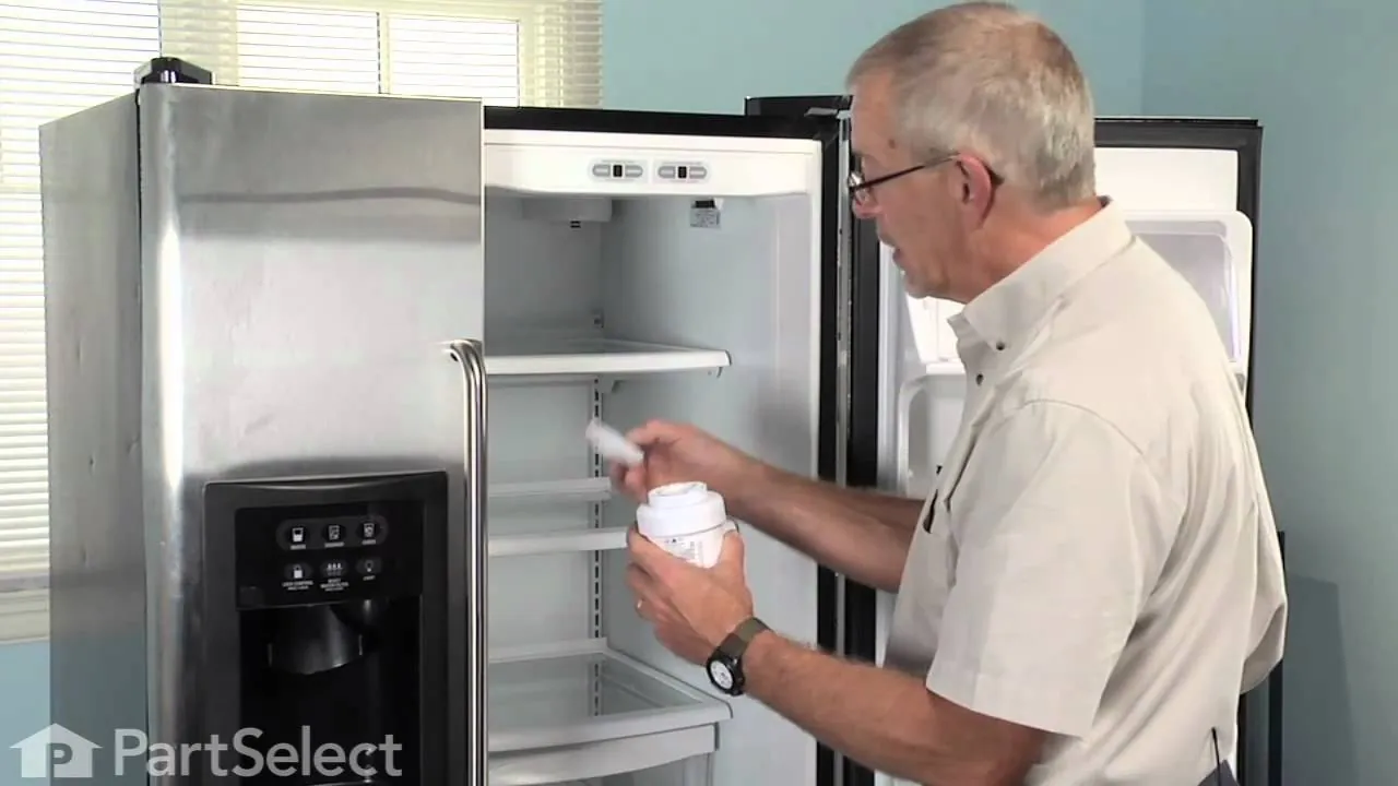 A technician cleaning dust from the condenser coils of a stainless steel refrigerator.