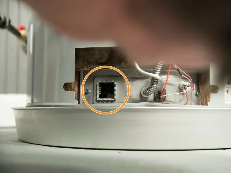 Technician inspecting the electronic ignition components inside a modern gas water heater unit.